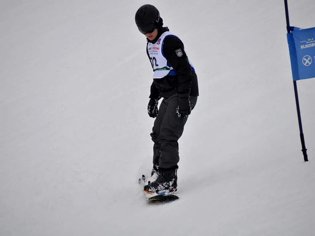 Snowboarder in dunkler Kleidung neben dem blauen Tor.